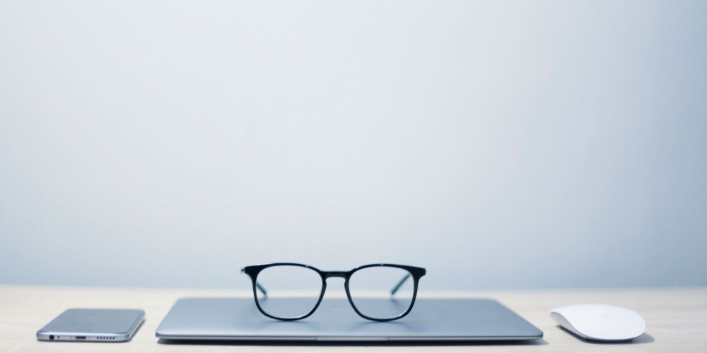 Glasses, laptop, smartphone, and mouse on desk.